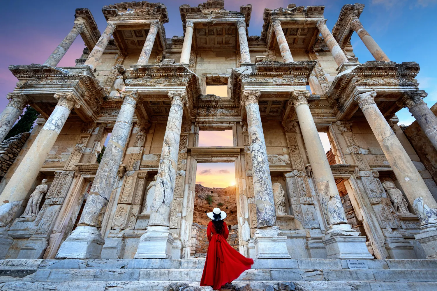 Woman in red dress looking at the Library of Celsus in Ephesus, Turkiye
