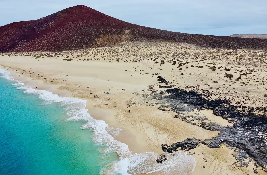 Beautiful beach with turqouise waters and desert in the background in La Graciosa