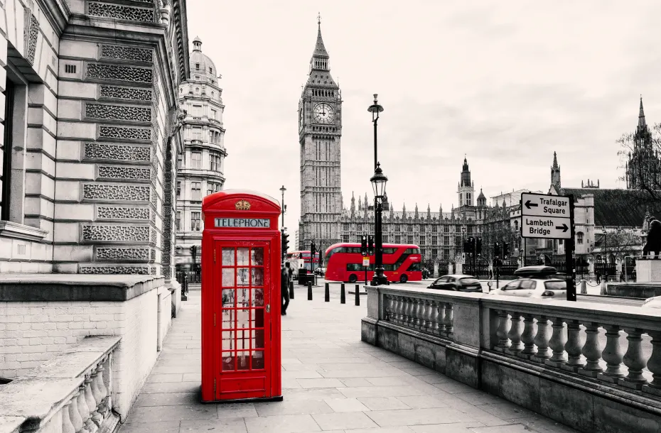 A black and white picture of London with a contrast of colors, coloring only a red telephone booth and a red bus