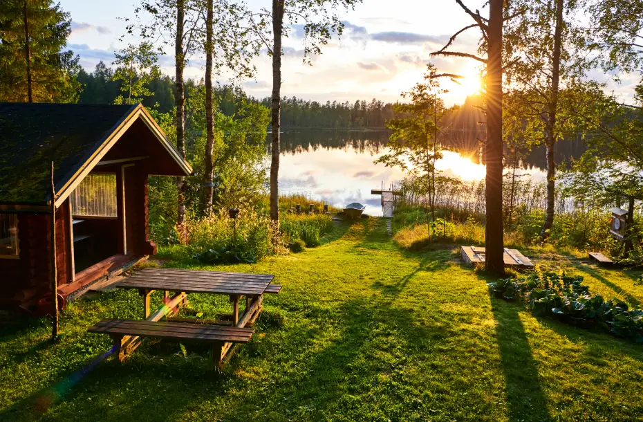 A wooden cabin in a green forest with a lake and a boat in Finland